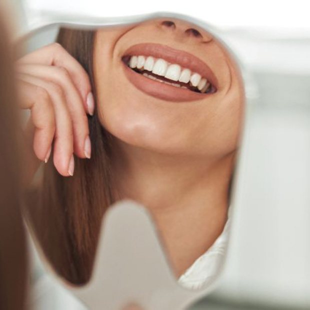 Dental patient’s smile reflected in hand mirror