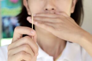 Woman covering her mouth while holding a toothpick 